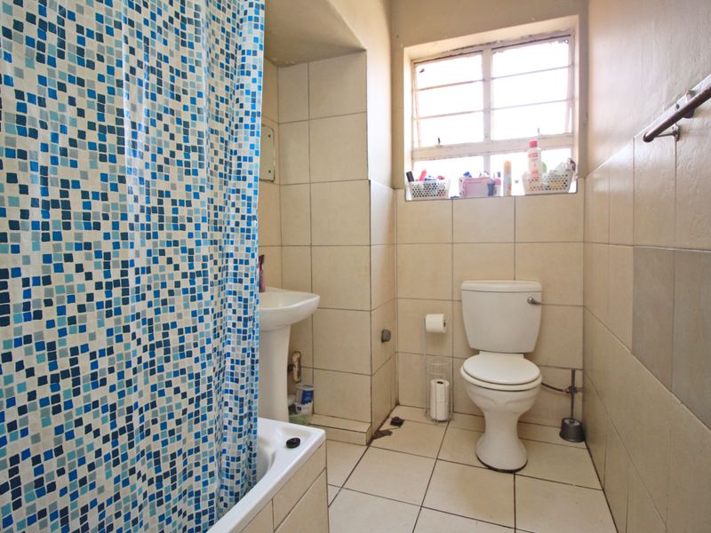 A functional bathroom featuring a pedestal sink, toilet, and tiled finishes, requiring cosmetic updates to improve its overall condition and aesthetic appeal.