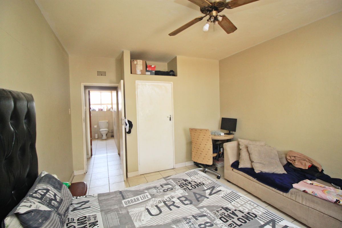 A bedroom featuring tiled flooring, a ceiling fan, and an en-suite bathroom access point, requiring cosmetic updates to improve its overall appeal.