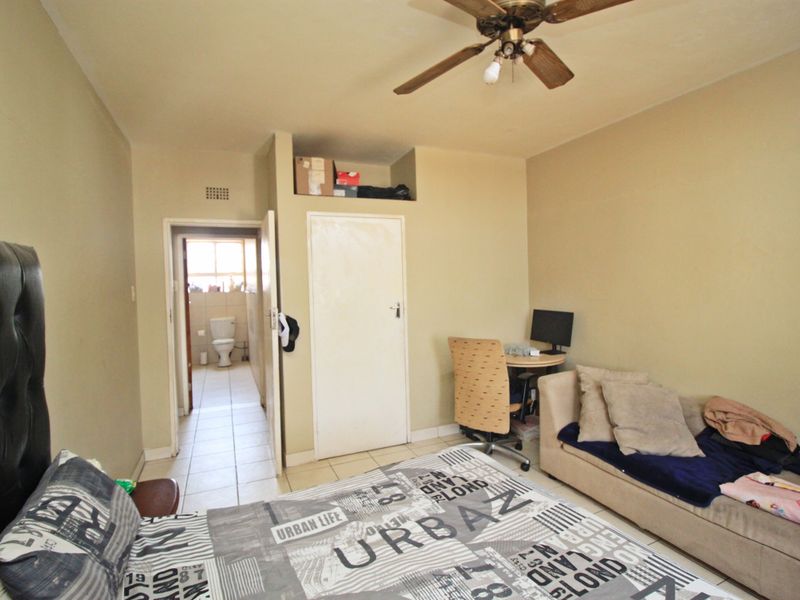 A bedroom featuring tiled flooring, a ceiling fan, and an en-suite bathroom access point, requiring cosmetic updates to improve its overall appeal.