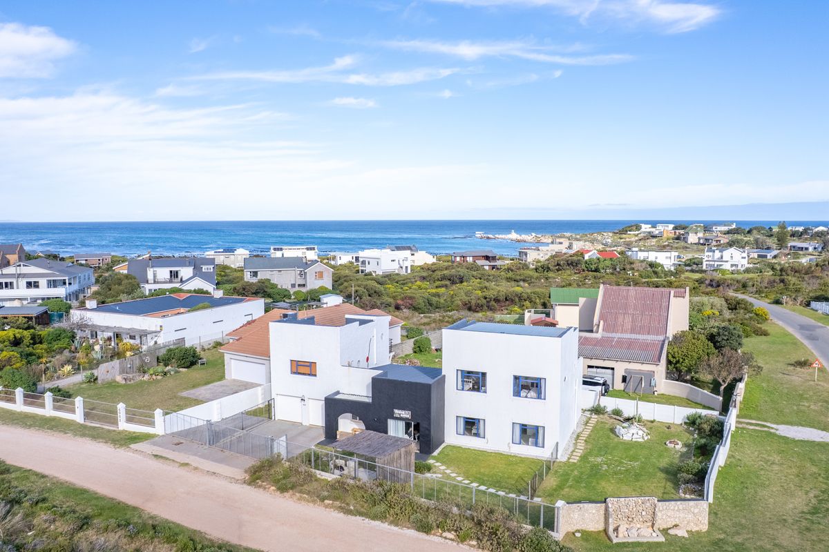 Aerial view of a modern two-story residential property featuring a white and black facade, landscaped garden, and boundary fencing, situated in a coastal neighborhood.