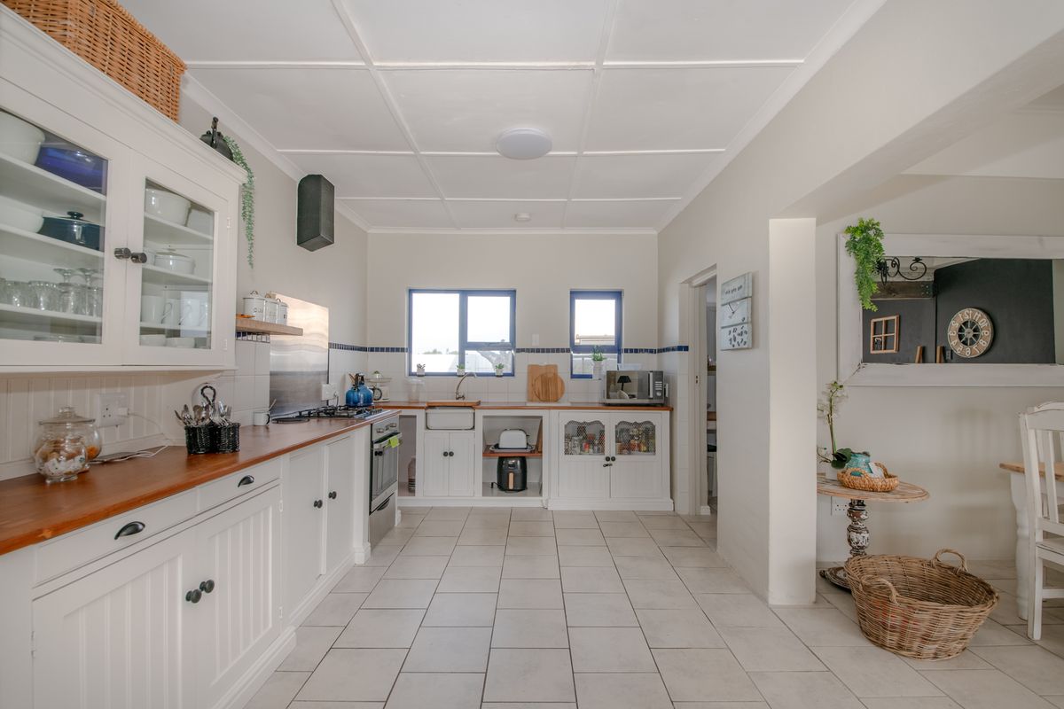 A bright, country-style kitchen featuring white cabinetry, wooden countertops, a farmhouse sink, and tiled flooring with an open-plan layout.