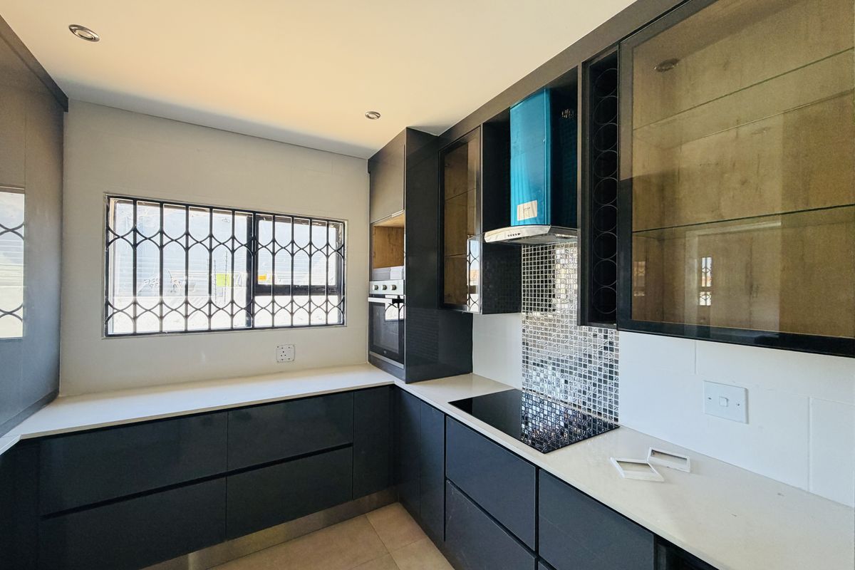 Modern kitchen featuring dark cabinetry, quartz countertops, mosaic tile backsplash, built-in oven, and electric hob with an extractor fan.