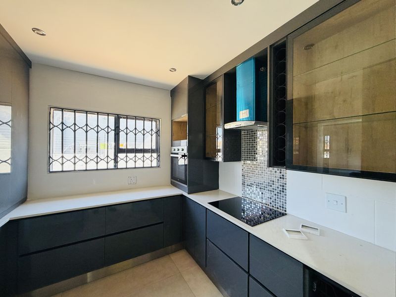 Modern kitchen featuring dark cabinetry, quartz countertops, mosaic tile backsplash, built-in oven, and electric hob with an extractor fan.