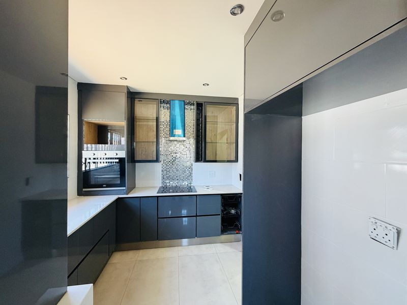 Modern kitchen featuring dark grey cabinetry, stone countertops, mosaic tile splashback, built-in oven, and electric hob with extractor fan.
