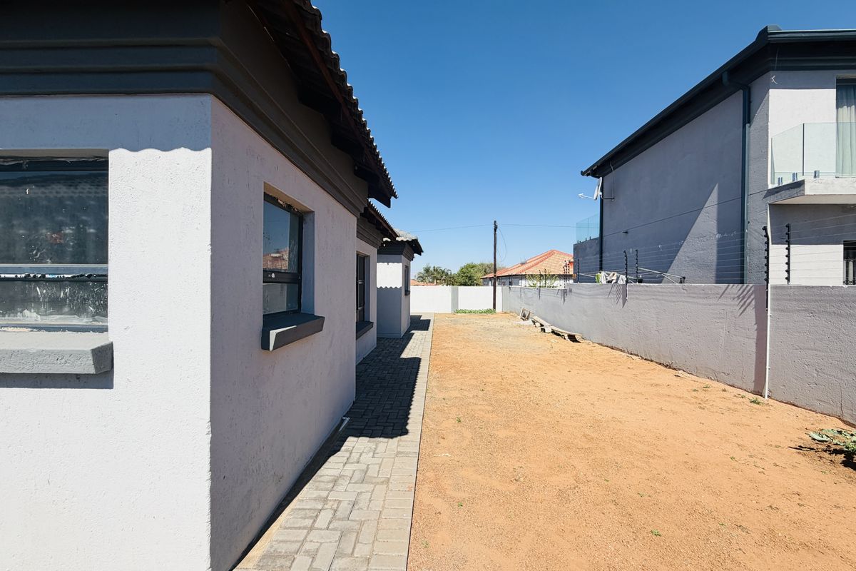 A side view of the property featuring a paved walkway alongside an unlandscaped rear yard enclosed by a perimeter wall with electric fencing.