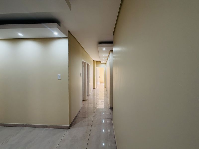 A clean, well-lit hallway featuring modern tiled flooring and recessed ceiling lighting with a decorative bulkhead design.