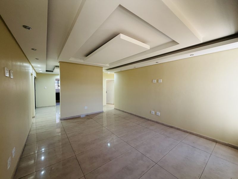 Spacious, empty living area featuring modern recessed ceiling design, tiled flooring, and integrated downlights, providing a clean and neutral canvas.