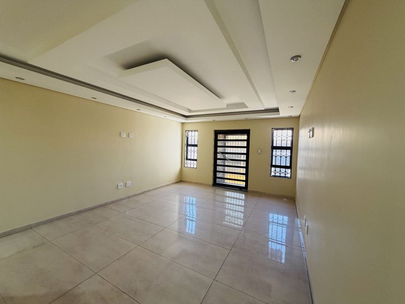 A bright, empty living room featuring modern recessed ceiling details, polished tile flooring, and secure metal-framed windows and entrance door.