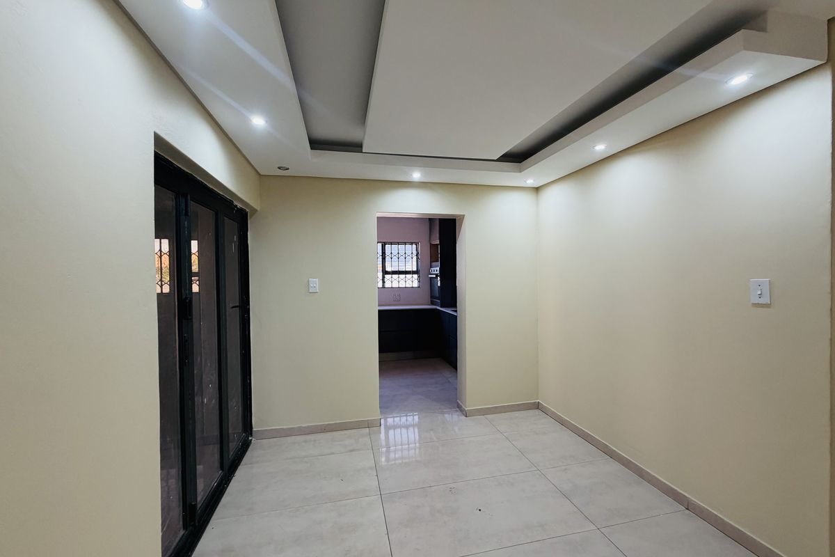 A bright, empty living area featuring modern recessed ceiling lighting, neutral tiled floors, and a sliding glass door leading to the exterior.