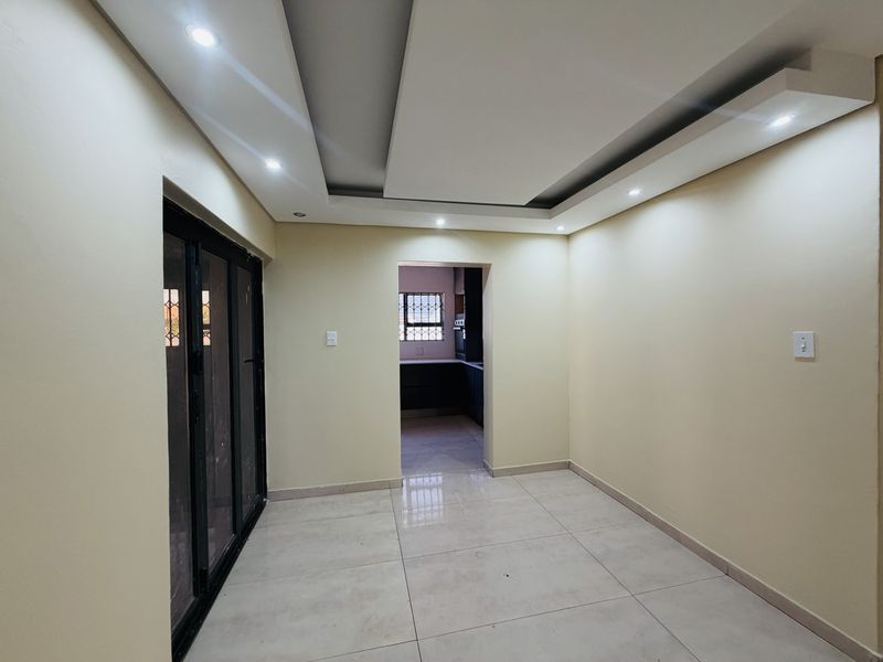 A bright, empty living area featuring modern recessed ceiling lighting, neutral tiled floors, and a sliding glass door leading to the exterior.