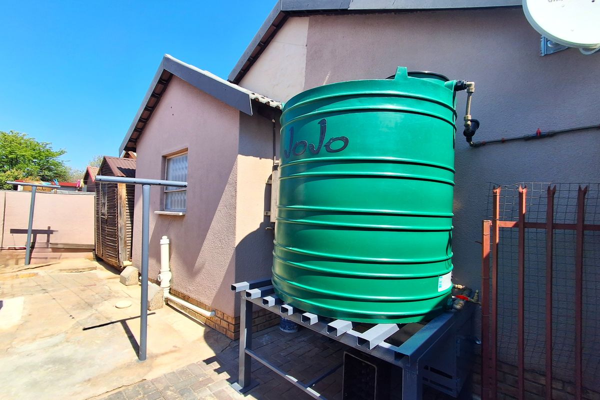 Rear exterior view featuring a green water storage tank on a metal stand, set against the side of the house with paved ground.