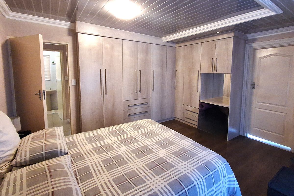 Spacious bedroom featuring extensive built-in cabinetry with a integrated vanity nook, laminate flooring, and a unique panelled ceiling with en-suite access.