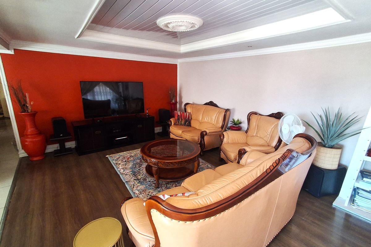 A spacious living room featuring a recessed ceiling with a decorative ceiling rose, downlights, and durable laminate flooring.