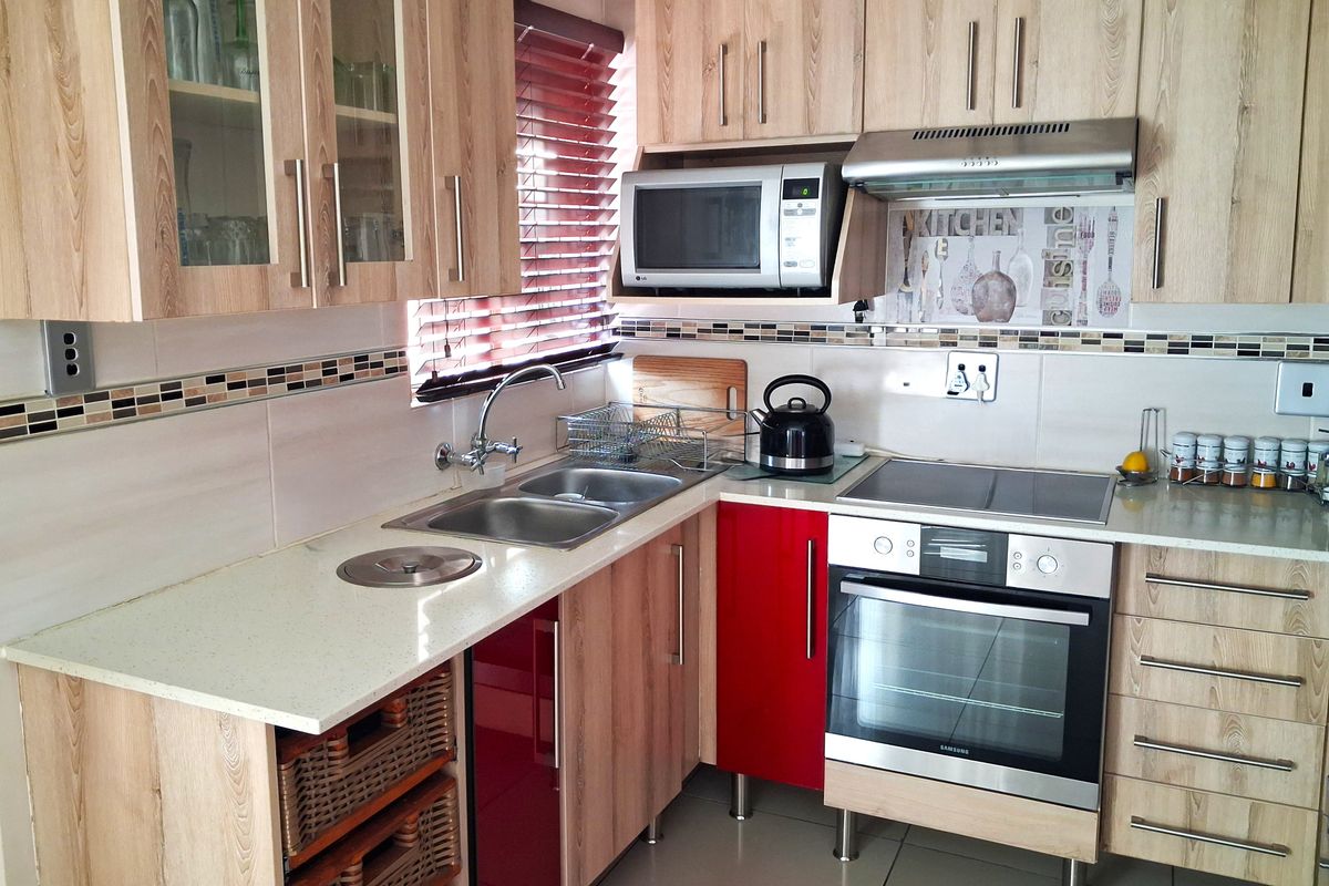 A functional kitchen featuring light wood-grain cabinetry, stone countertops, a built-in oven, electric hob, and a tiled backsplash with decorative accents.