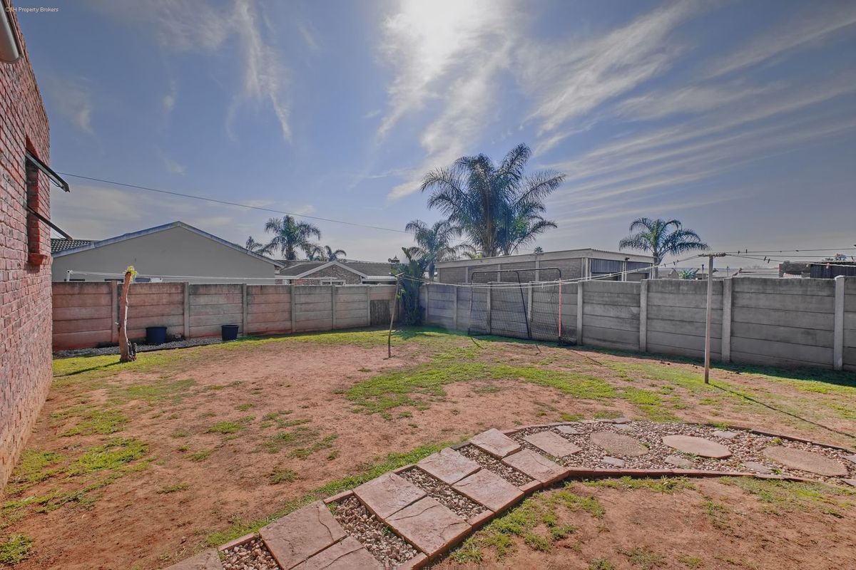 A rear garden area featuring a precast concrete boundary wall, a stone paver pathway, and an open lawn space.