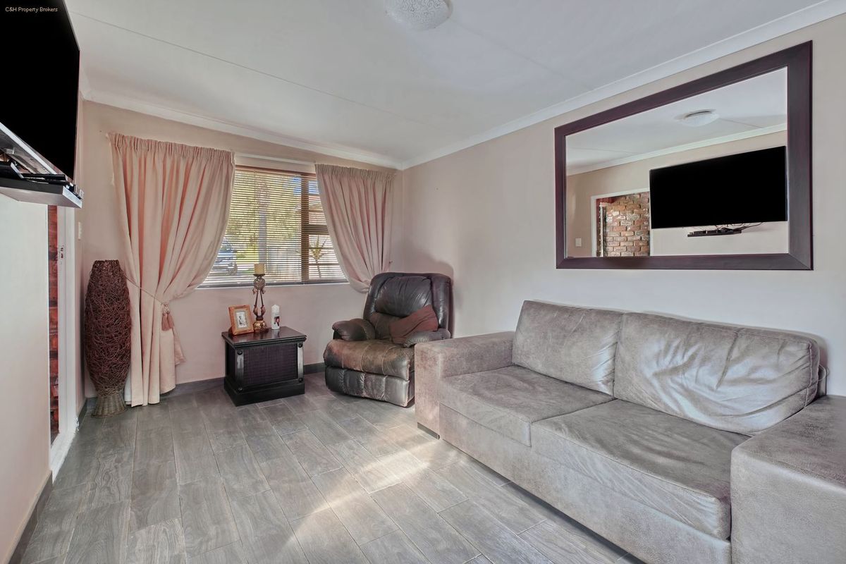 A comfortable living room featuring tiled flooring, a large window with curtains, and a ceiling rose, providing a functional and well-lit space.