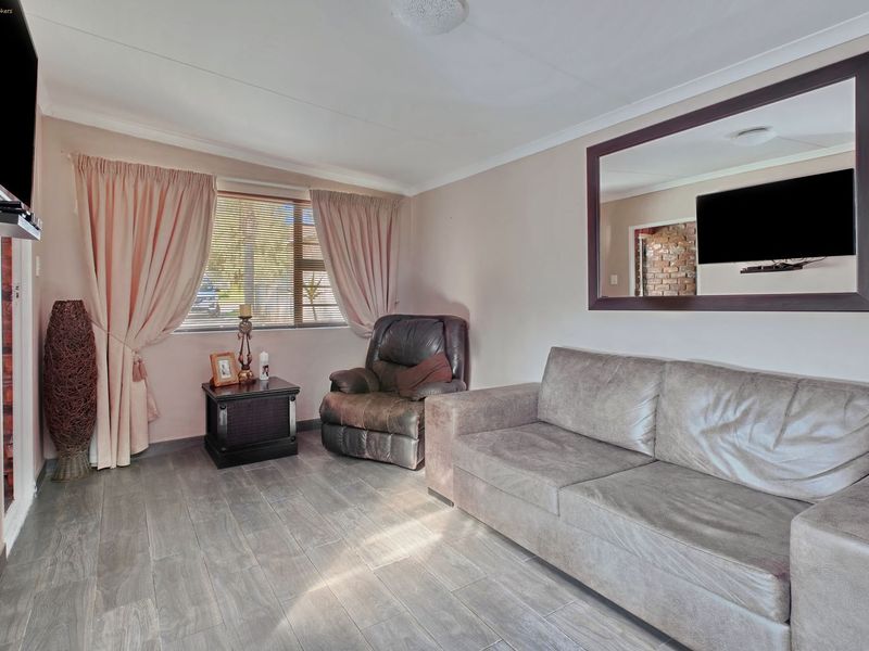 A comfortable living room featuring tiled flooring, a large window with curtains, and a ceiling rose, providing a functional and well-lit space.