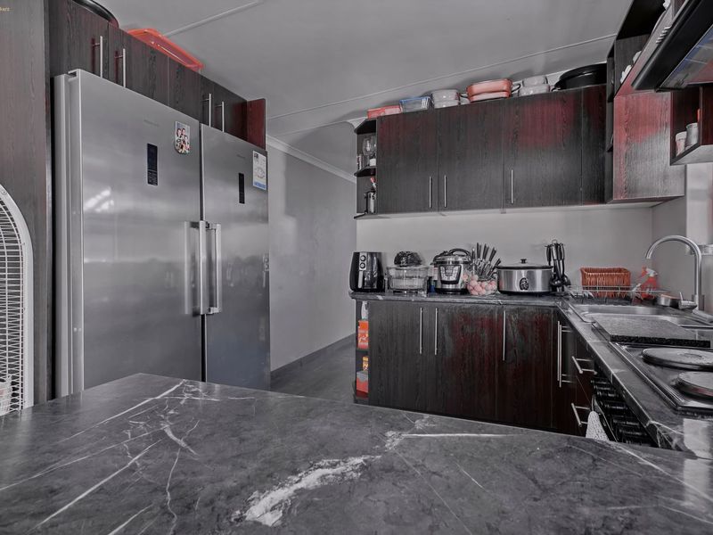 A functional kitchen featuring dark wood cabinetry, marble-look countertops, and integrated stainless steel appliances.