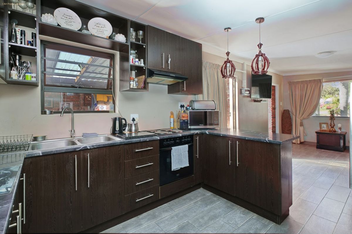 A functional kitchen featuring dark wood cabinetry, laminate countertops, built-in oven, electric hob, and tiled flooring, seamlessly flowing into the adjacent living area.