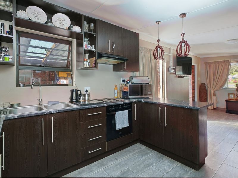 A functional kitchen featuring dark wood cabinetry, laminate countertops, built-in oven, electric hob, and tiled flooring, seamlessly flowing into the adjacent living area.
