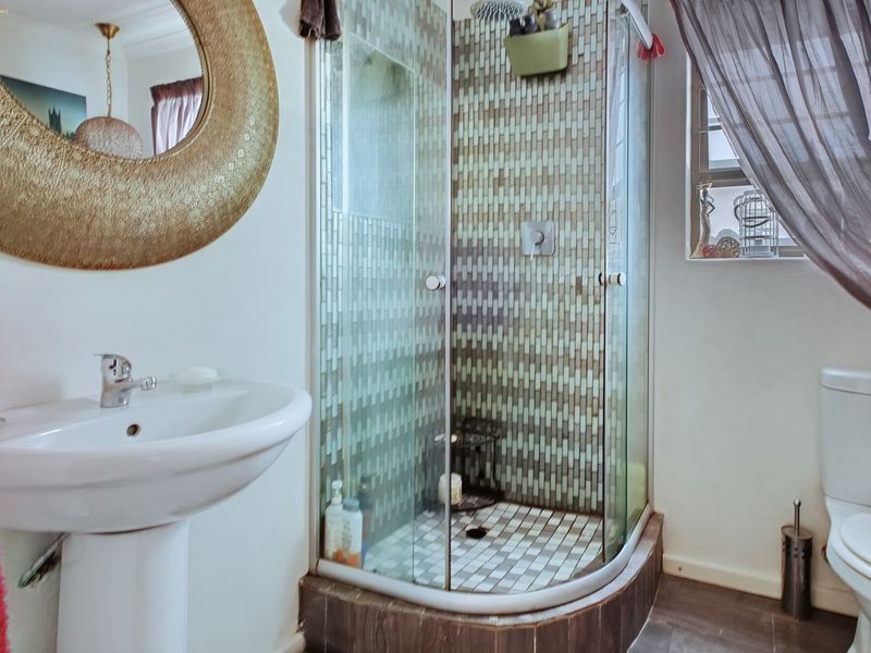 A functional bathroom featuring a corner shower enclosure with mosaic tiling, a pedestal basin, and a standard toilet.
