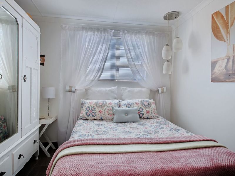 A cozy bedroom featuring neutral walls, a window with venetian blinds, and modern pendant lighting.