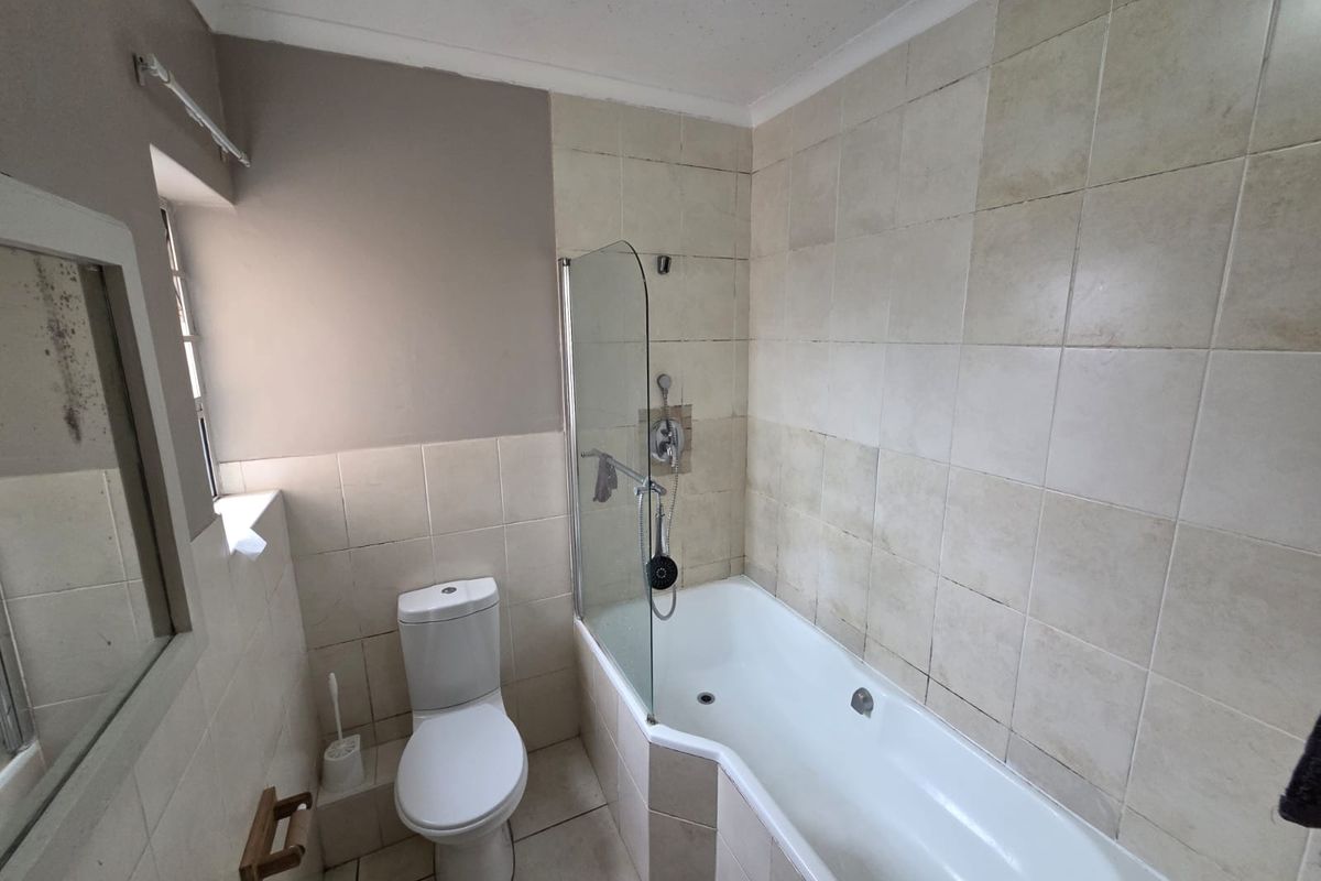 A functional bathroom featuring a bathtub with a glass shower screen, tiled walls, and a standard toilet.