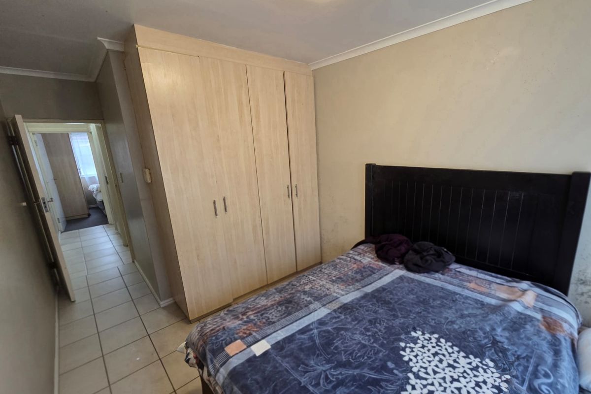 A bedroom featuring built-in wooden wardrobes and tiled flooring, showing signs of wear on the walls requiring maintenance and cosmetic updates.