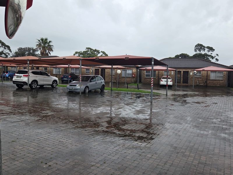 Exterior view of an apartment complex featuring a paved parking area with covered carports and brick building facades.