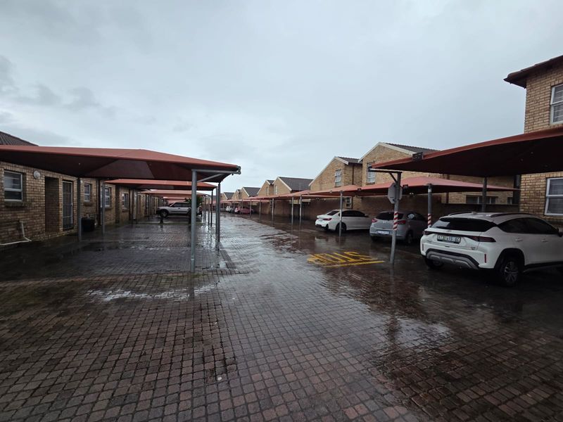 Exterior view of an apartment complex featuring a paved driveway with covered parking bays and brick building facades.