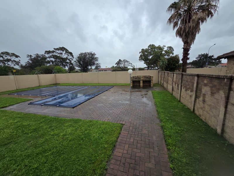 Outdoor pool area featuring a covered swimming pool, brick paved patio, and a built-in braai, enclosed by perimeter walls.