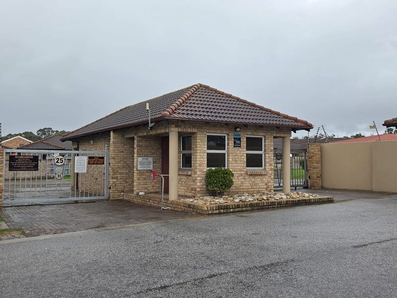 A secure entrance gatehouse featuring brick construction, a tiled roof, and automated security gates for the apartment complex.