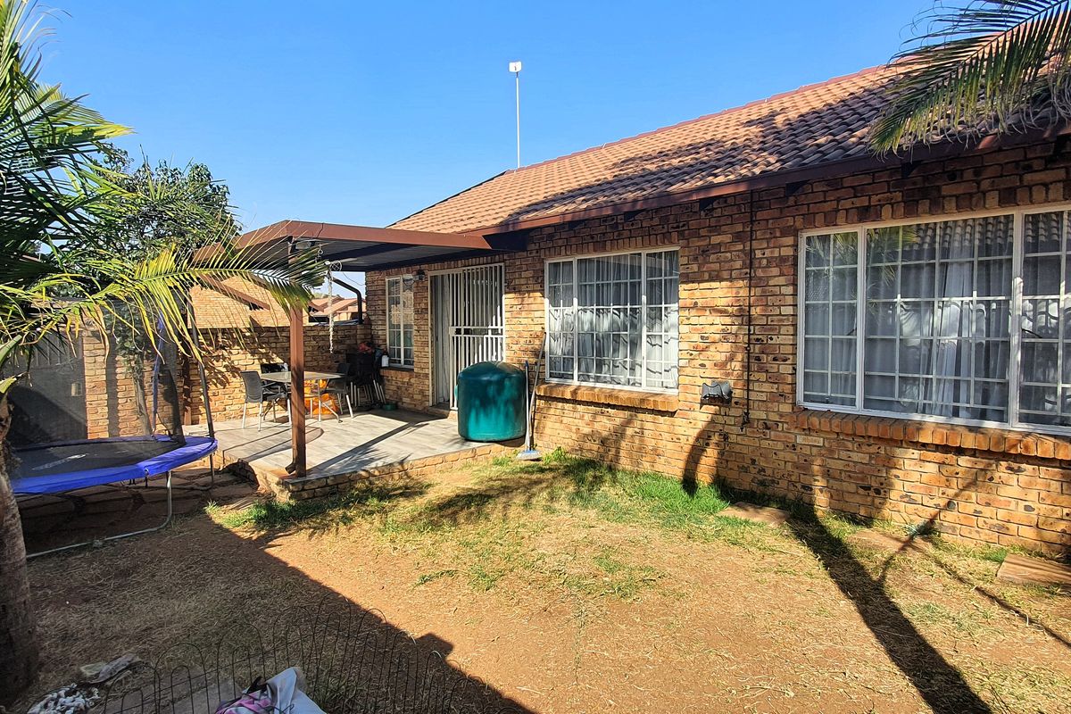 Rear view of the townhouse featuring a brick facade, tiled roof, and a covered patio area overlooking a private garden space.