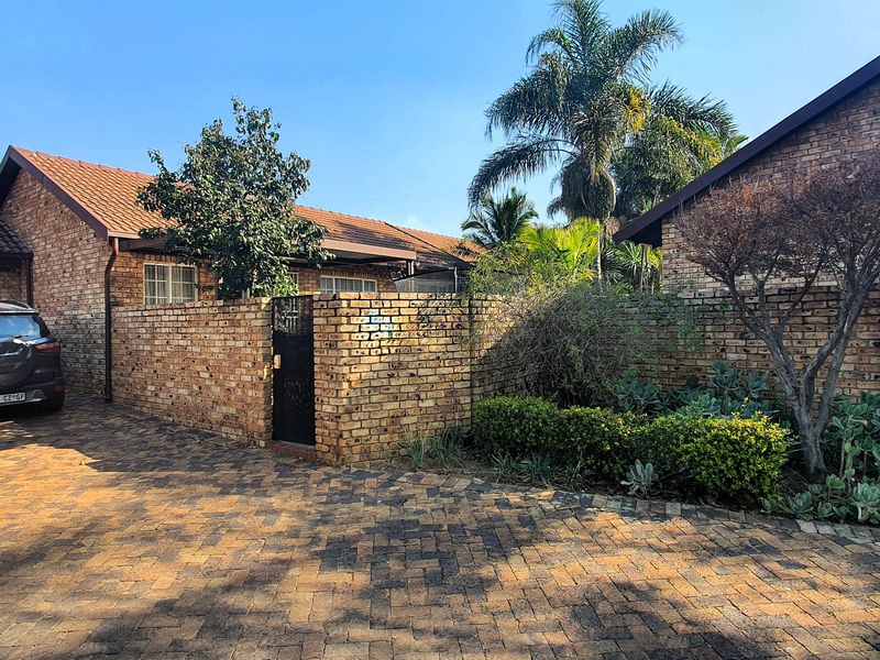 Front exterior view of a face brick townhouse featuring a paved driveway, secure boundary wall, and private garage access.