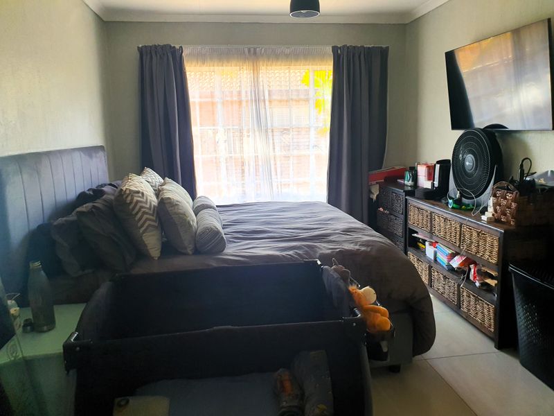 A functional bedroom featuring tiled flooring and natural light through a window with curtain rails.