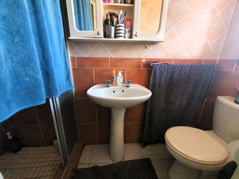 A functional bathroom featuring a pedestal basin, toilet, and shower enclosure with dated ceramic wall and floor tiling.