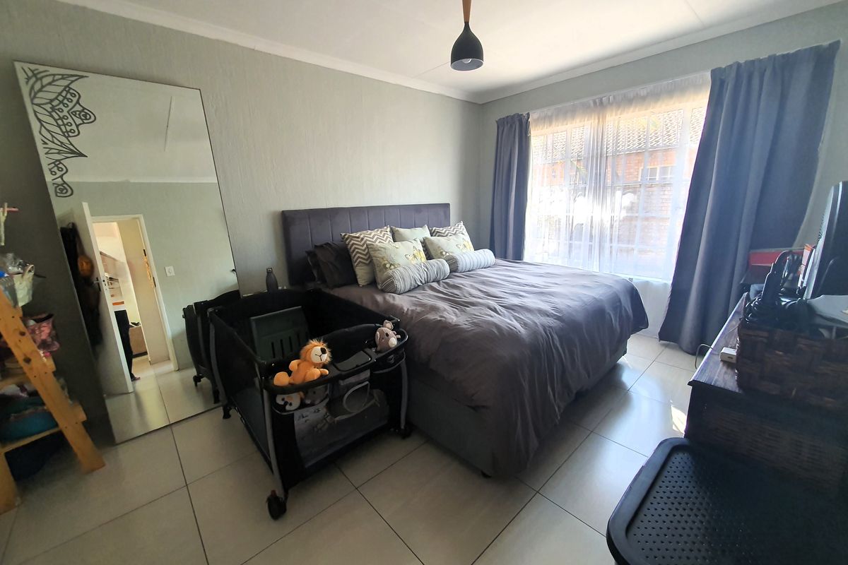 A well-lit bedroom featuring neutral tiled flooring, a central pendant light, and a large window with curtains.