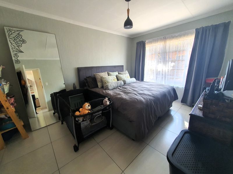 A well-lit bedroom featuring neutral tiled flooring, a central pendant light, and a large window with curtains.