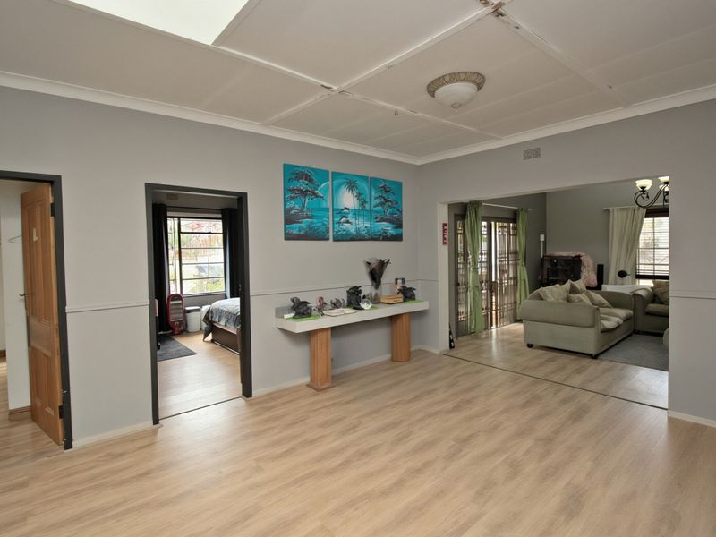 Spacious open-plan living area featuring light-toned laminate flooring, neutral wall finishes, and a multi-room layout with direct access to adjacent living and bedroom spaces.
