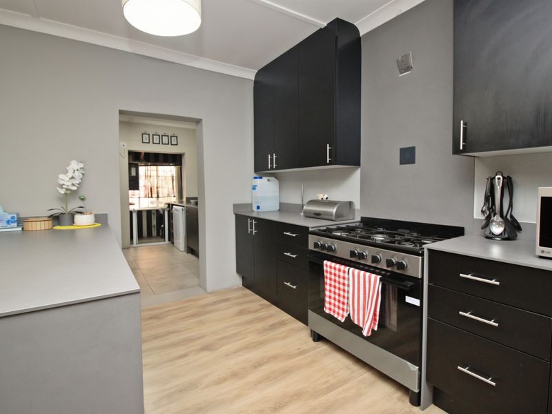 Modern kitchen featuring dark cabinetry, gas stove, oven, and light wood-look laminate flooring, with an adjacent scullery area visible through the doorway.