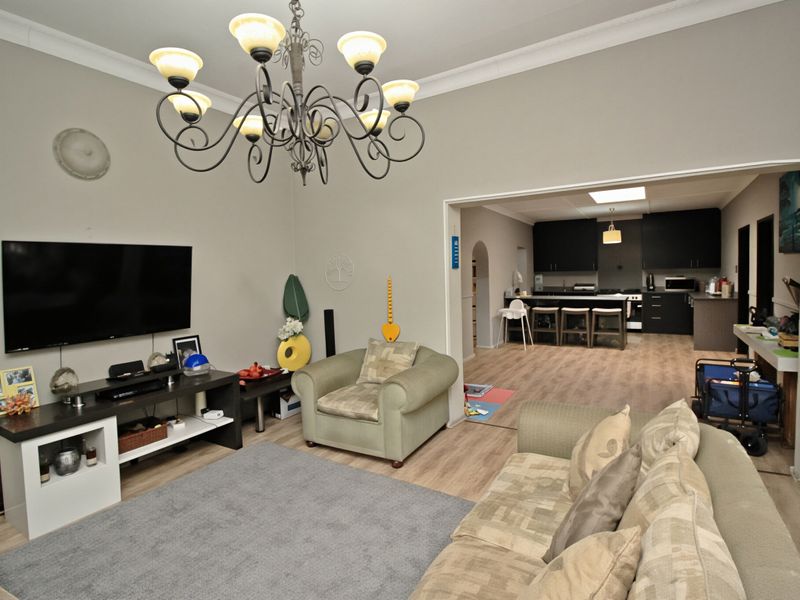 Open-plan living area featuring laminate flooring and cove cornicing, flowing into a modern kitchen with dark cabinetry and a central island.