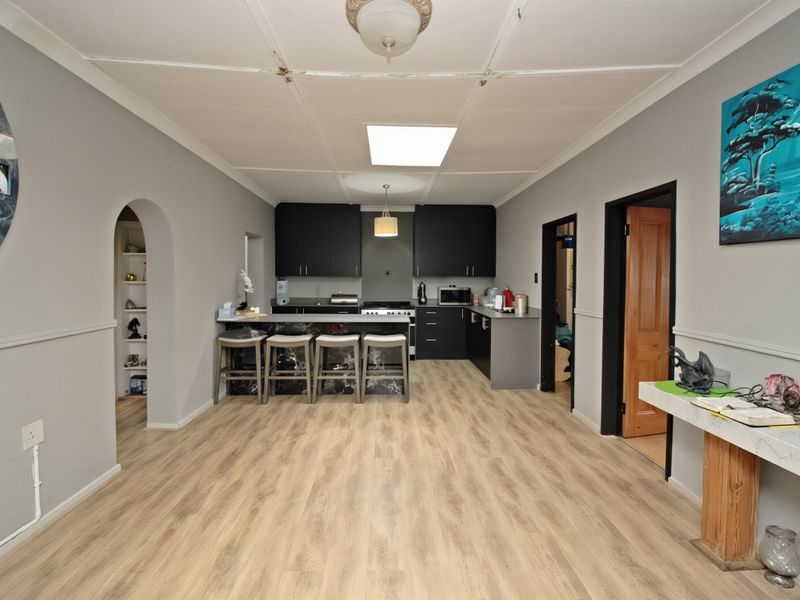 Open plan kitchen and living area featuring modern dark cabinetry, a central island, and light wood-look laminate flooring.