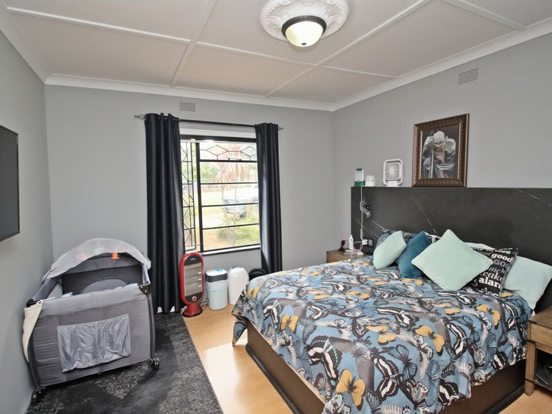 A well-maintained bedroom featuring laminate flooring, a decorative ceiling rose with a central light fixture, and a modern built-in headboard.