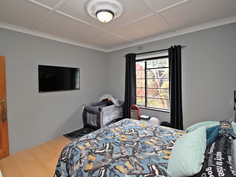 A bedroom featuring a coffered ceiling with a decorative ceiling rose, timber door, and a window fitted with a security gate.