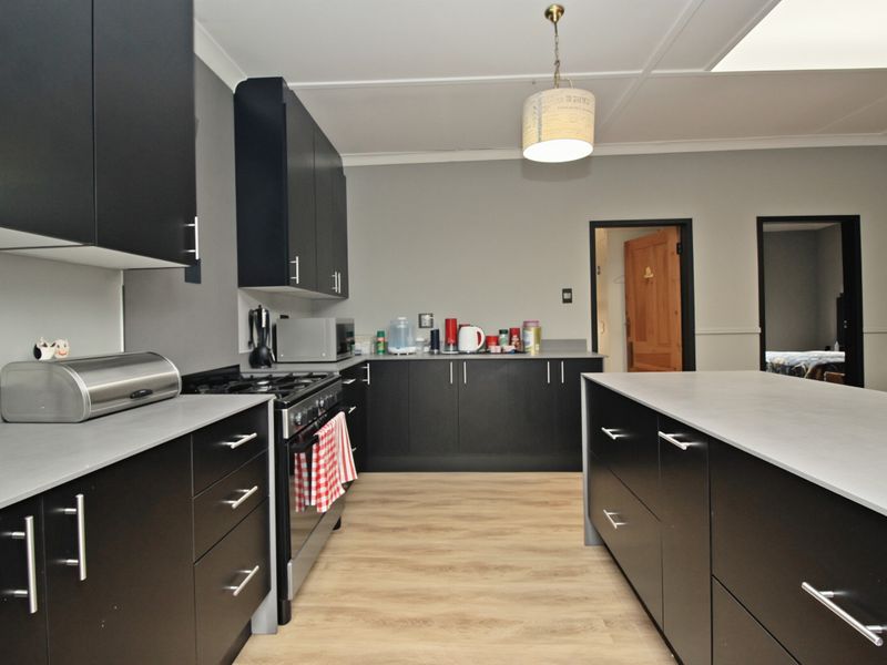 Modern kitchen featuring sleek black cabinetry, light grey countertops, a central island, and a freestanding gas stove with wood-look laminate flooring.