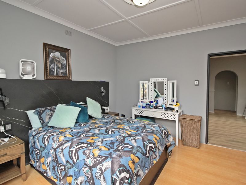 A bedroom featuring laminate flooring, a coffered ceiling, and a dark feature wall panel behind the bed area.