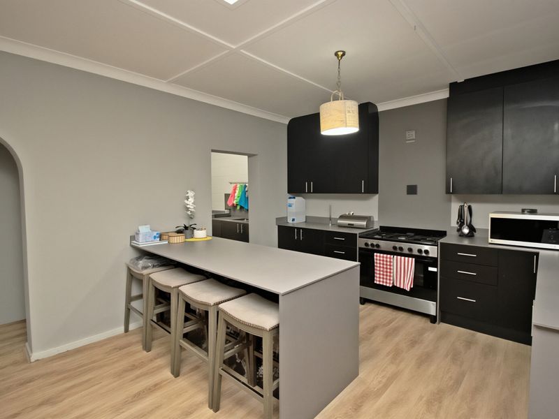 Modern kitchen featuring dark cabinetry, a central island with breakfast bar seating, gas stove, and light wood-look laminate flooring.
