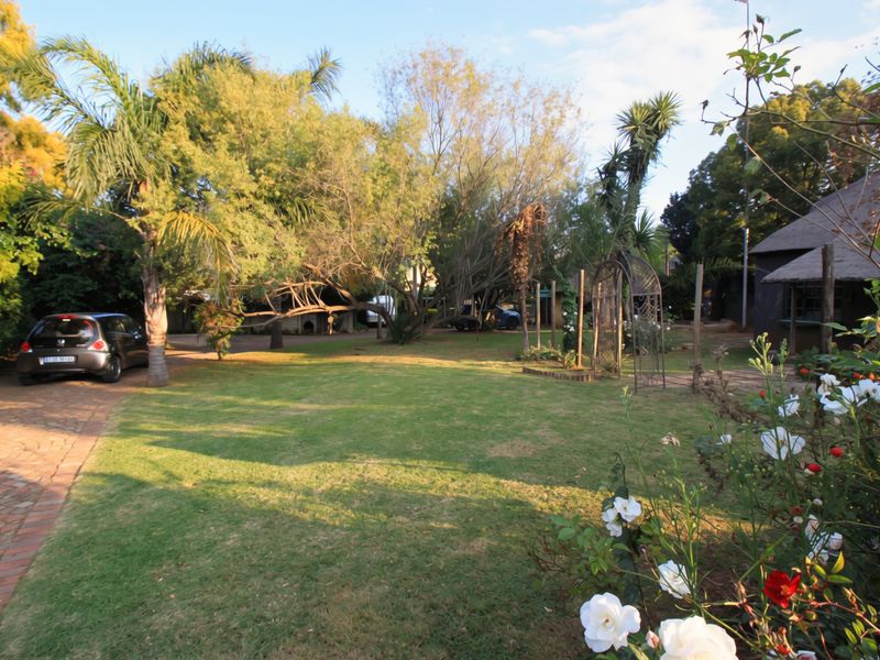 A spacious, well-maintained garden featuring a brick-paved driveway, mature trees, and a decorative metal garden arch.
