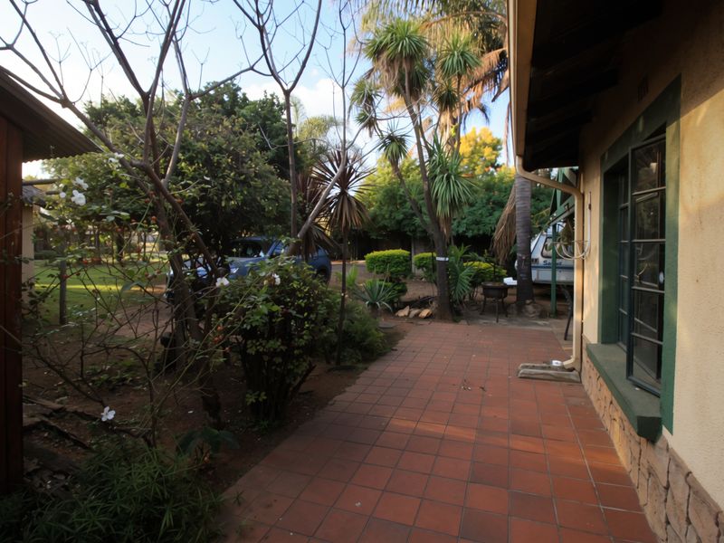 A rear exterior view featuring a tiled patio area adjacent to the house, with established garden landscaping and mature trees.