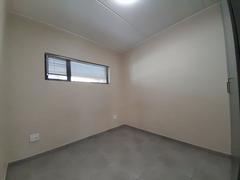 A clean, empty bedroom featuring neutral wall paint, tiled flooring, a built-in cupboard, and a window fitted with horizontal blinds.